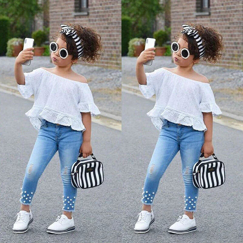 Girl in off-shoulder white lace top, blue skinny jeans with pearl details, and white sneakers