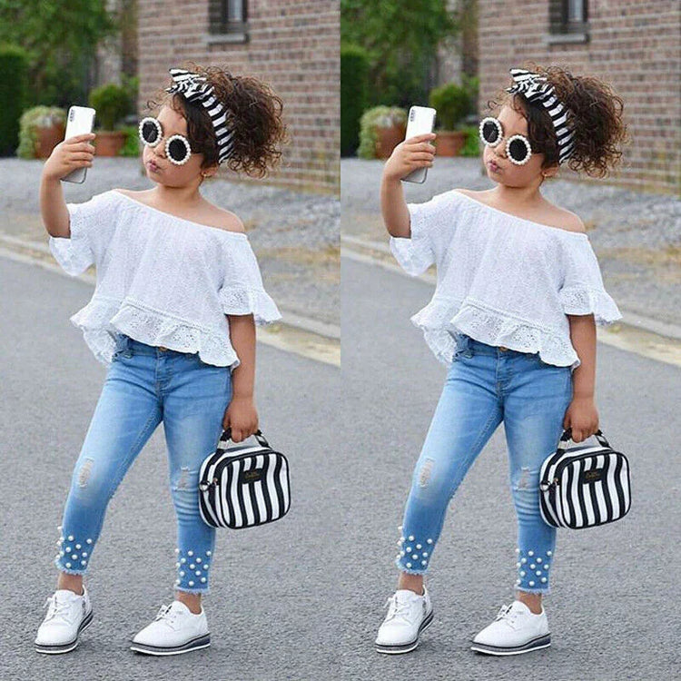 Girl in off-shoulder white lace top, blue skinny jeans with pearl details, and white sneakers