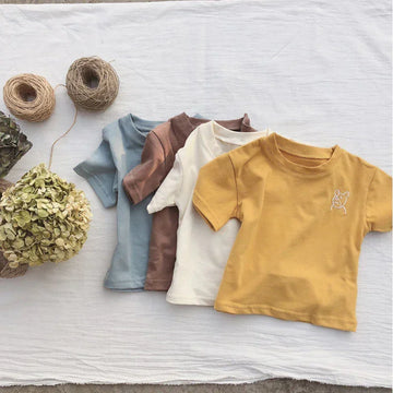 Four short-sleeve cotton t-shirts in pastel yellow, cream, brown, and blue, laid flat