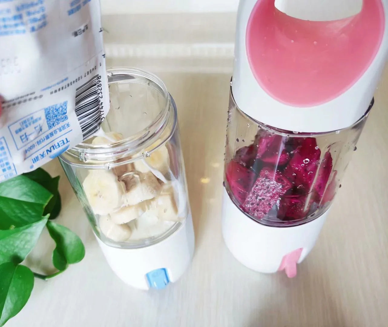 Two portable blenders with chopped fruit, one with bananas, one with red dragon fruit.