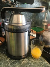 Stainless steel electric juicer with a glass of fresh orange juice on a kitchen counter
