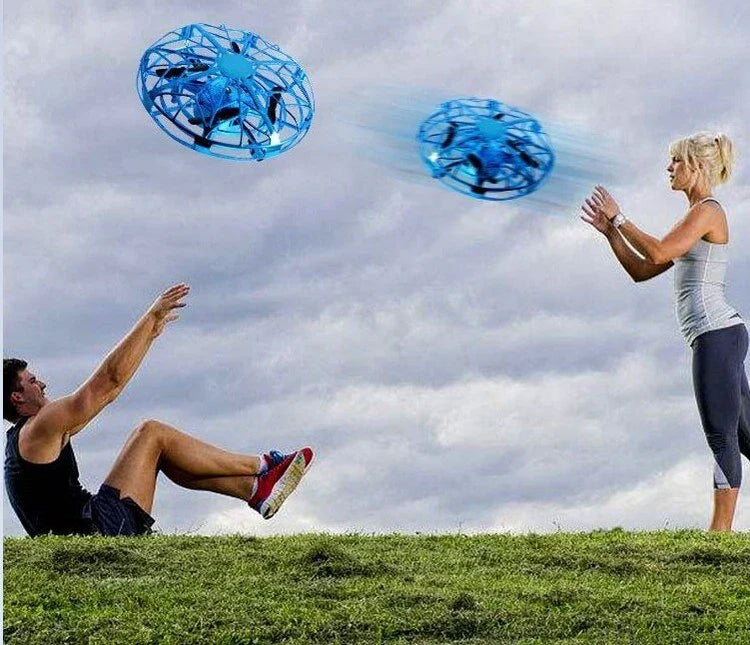 Man in black athletic shorts and tank, woman in gray fitted leggings and top, playing with blue flying drones outdoors.