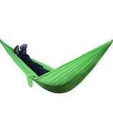 Person wearing dark pants and sneakers relaxing in a bright green nylon hammock