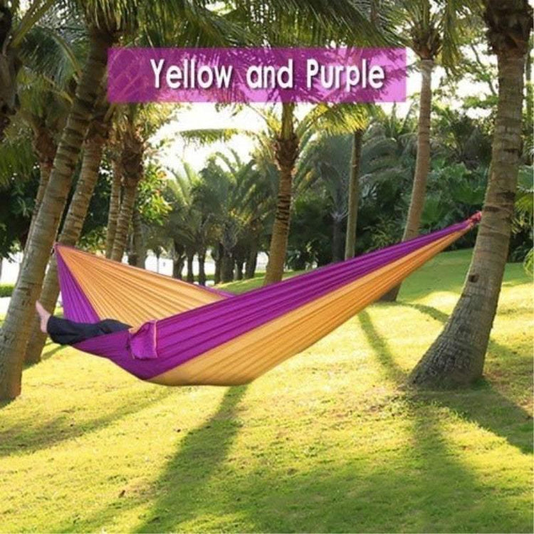 Person relaxing in a yellow and purple nylon hammock between palm trees outdoors