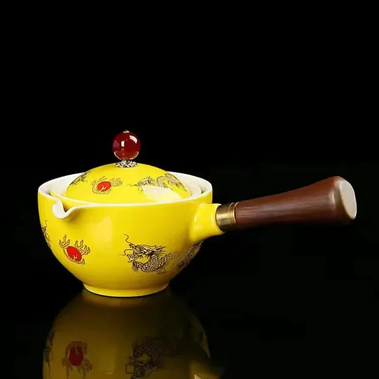 Yellow ceramic teapot with dragon design, wooden handle, and red knob lid on black background