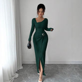 Woman wearing a fitted dark green ribbed maxi dress with long sleeves and front slit