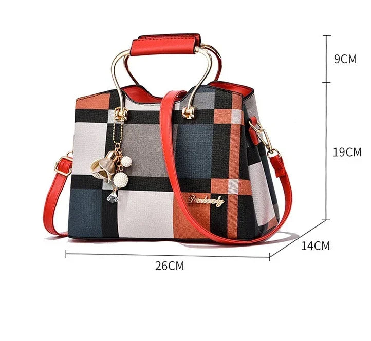Plaid handbag with red leather trim, gold hardware, top handle, crossbody strap, and charm accent