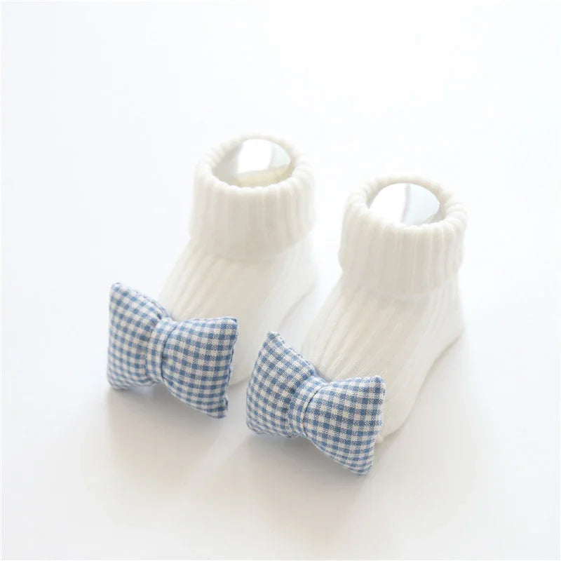 White ribbed knit baby socks with blue gingham bow accents, soft and snug fit.