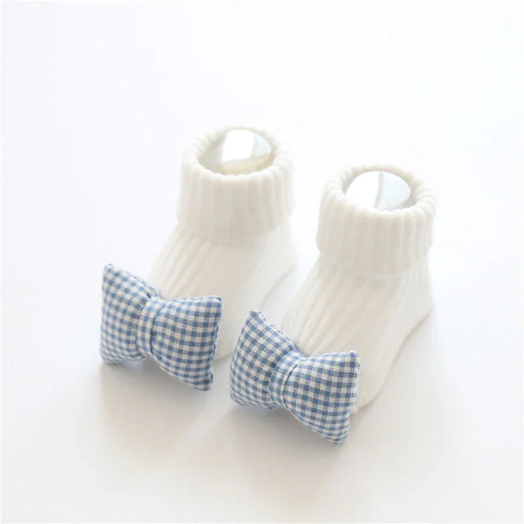 White ribbed knit baby socks with blue gingham bow accents, soft and snug fit.