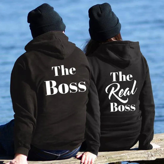 Couple wearing black hoodies with white slogan lettering, relaxed fit, casual streetwear style.