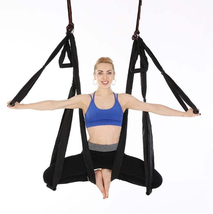 Woman in blue sports bra and black leggings doing aerial yoga in black hammock