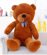 Large brown plush teddy bear with soft fabric and plaid bow tie sitting on a sofa