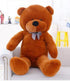 Large brown plush teddy bear with soft fabric and plaid bow tie sitting on a sofa