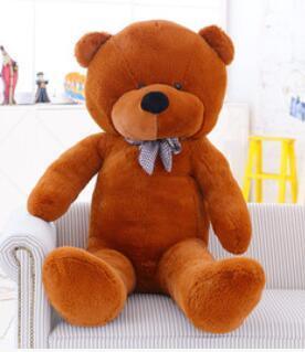 Large brown plush teddy bear with soft fabric and plaid bow tie sitting on a sofa
