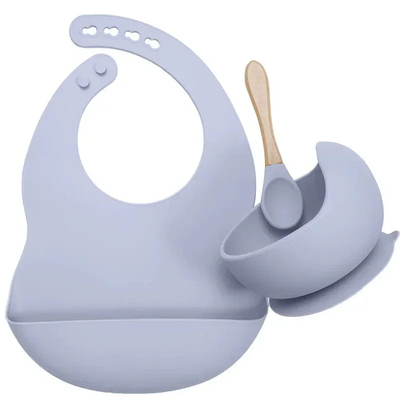 Light purple silicone bib, bowl, and spoon set with wooden handle, modern minimalist design.