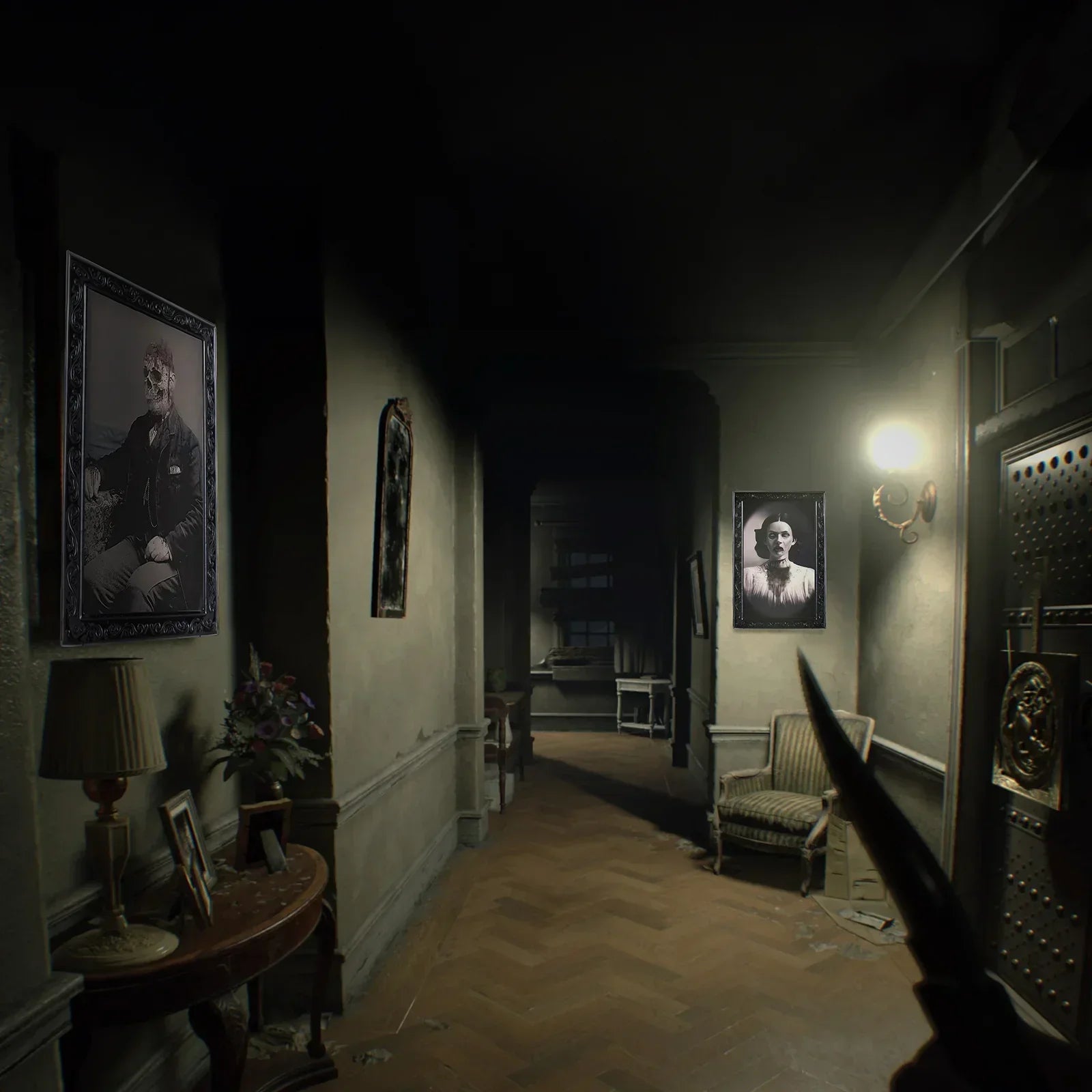 Dimly lit hallway with vintage portraits, patterned chair, wooden floor, and ornate decor.