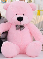 Large plush pink teddy bear with black bow tie, soft fuzzy fabric, sitting upright indoors