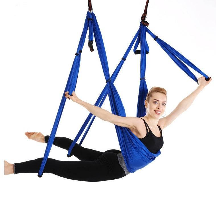 Woman in black fitted activewear using a blue aerial yoga hammock, demonstrating a stretch pose