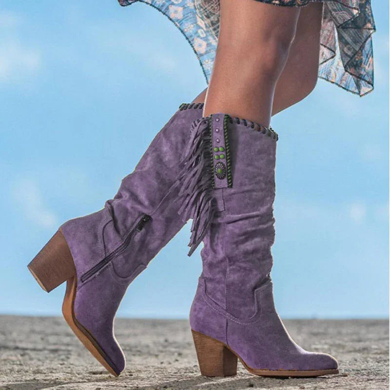 Woman wearing tall purple suede boots with fringe detailing and chunky heels outdoors