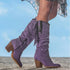 Woman wearing tall purple suede boots with fringe detailing and chunky heels outdoors