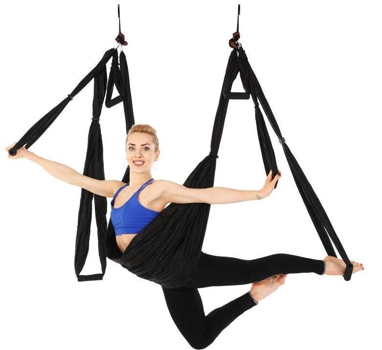 Woman in blue sports bra and black leggings practicing aerial yoga in black hammock