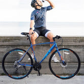 Man in fitted geometric print cycling jersey and black and gray shorts, wearing helmet, sitting on a ledge next to a blue road bike.