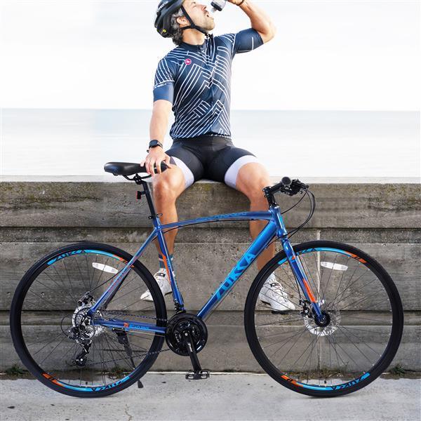 Man in fitted geometric print cycling jersey and black and gray shorts, wearing helmet, sitting on a ledge next to a blue road bike.