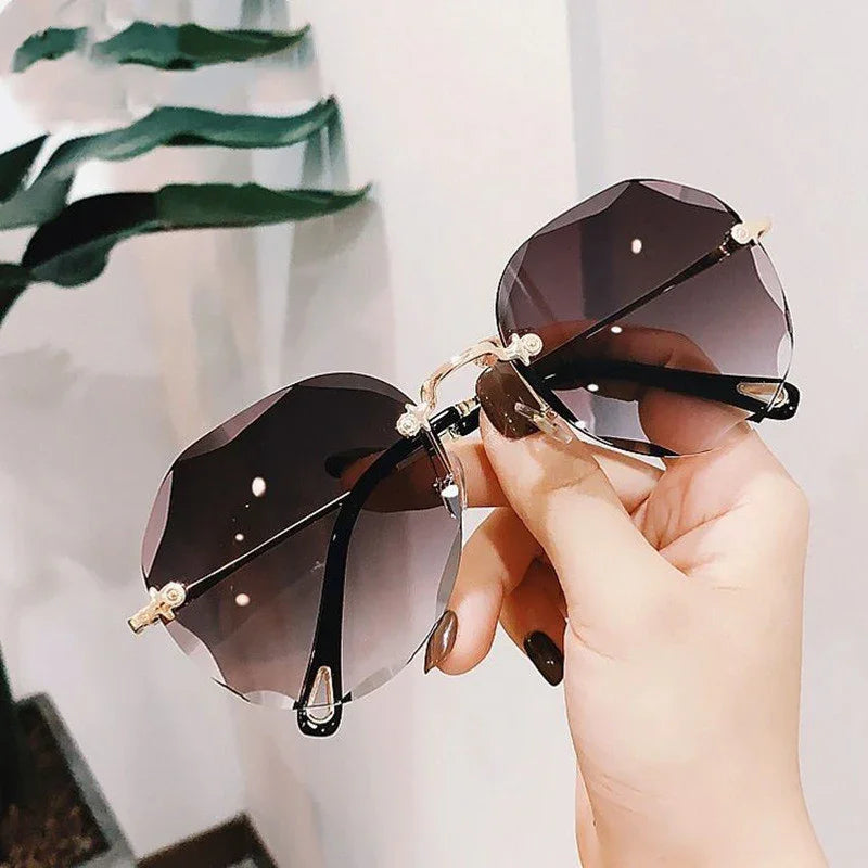 Hand holding oversized rimless sunglasses with dark gradient lenses and gold metal accents