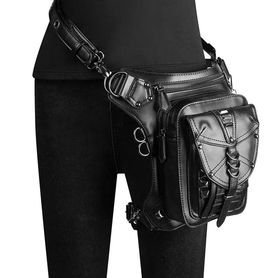 Black faux leather utility belt bag with silver hardware, worn over black skinny jeans
