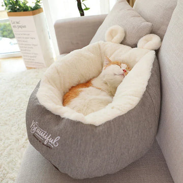 Cat sleeping in a plush, grey and white faux fur pet bed with ear-shaped accents