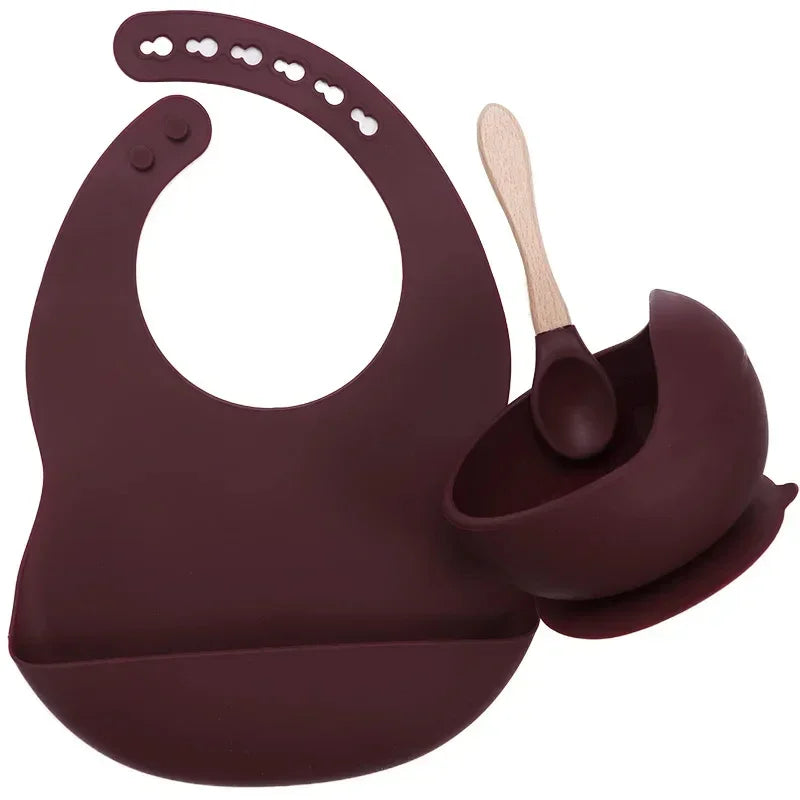 Dark maroon silicone bib, matching suction bowl, and wooden-handled spoon feeding set