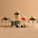Set of translucent baby bottles and pacifiers in beige and orange with ergonomic handles on a neutral background