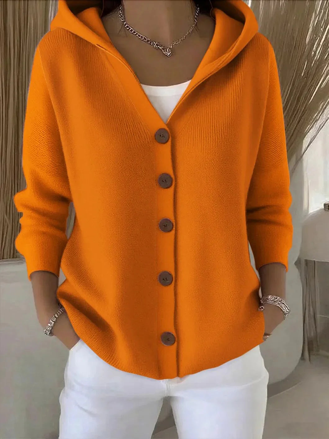 Woman wearing an orange knit hooded cardigan with buttons, relaxed fit, paired with white pants