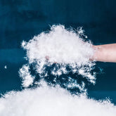 Hand holding soft white down filling material for puffer jackets against blue background