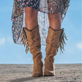 Tan suede fringe mid-calf boots with relaxed fit, paired with a patterned sheer skirt outdoors