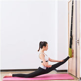 Woman in black leggings and white sports bra doing splits stretch with yoga strap on door