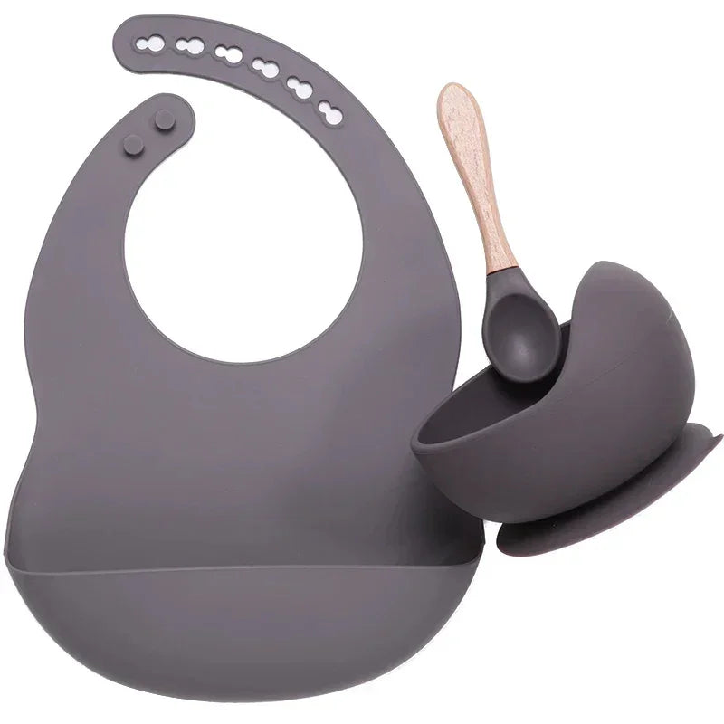 Gray silicone baby bib with matching bowl and wooden-handled spoon, modern feeding set