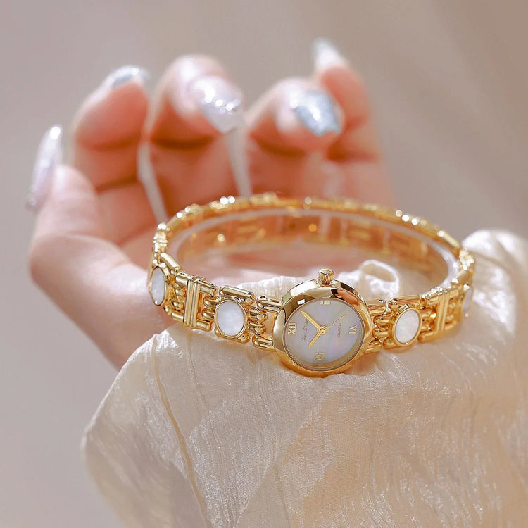 Gold bracelet watch with white face and mother of pearl accents, elegant satin sleeve