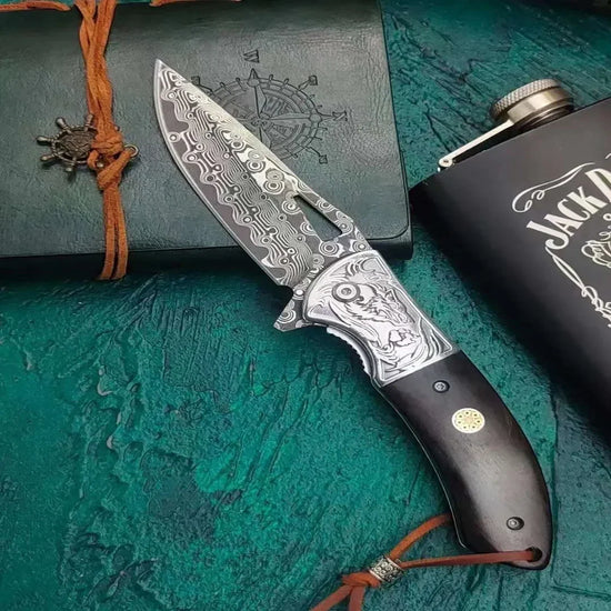 Ornate Damascus steel folding knife with engraved patterns and dark wood handle on textured background.