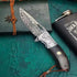 Ornate Damascus steel folding knife with engraved patterns and dark wood handle on textured background.
