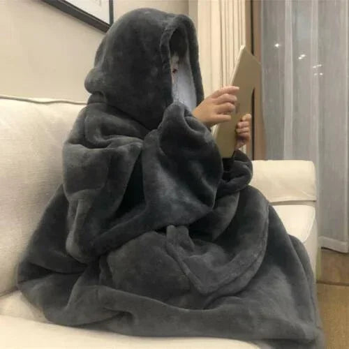 Person on sofa wearing oversized dark gray fleece hooded blanket, relaxed fit, cozy loungewear