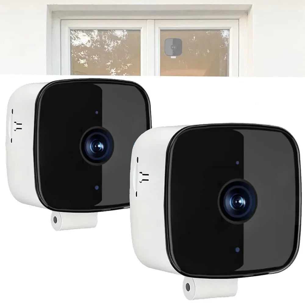 Two black and white compact security cameras with glossy finish, shown indoors and mounted on a window.