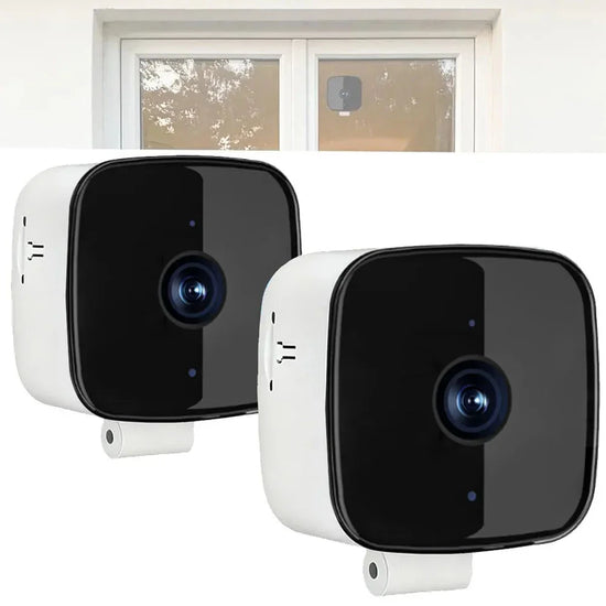 Two black and white compact security cameras with glossy finish, shown indoors and mounted on a window.
