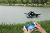 Person using smartphone to control a black and teal remote control boat on a lake