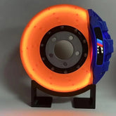 Futuristic glowing orange disc brake lamp with blue caliper on a black stand, modern decor