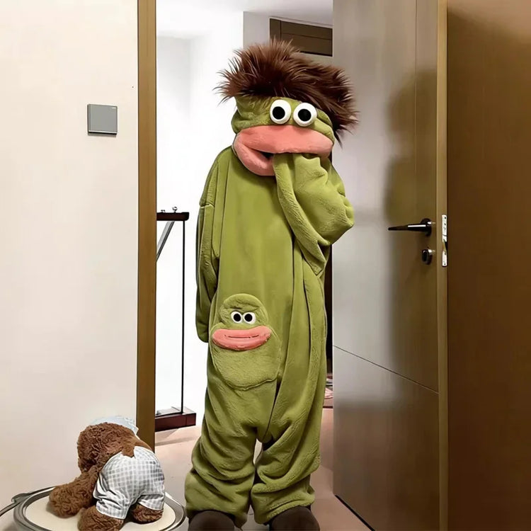 Person wearing oversized green plush onesie with cartoon face, relaxed fit, and fuzzy hood.