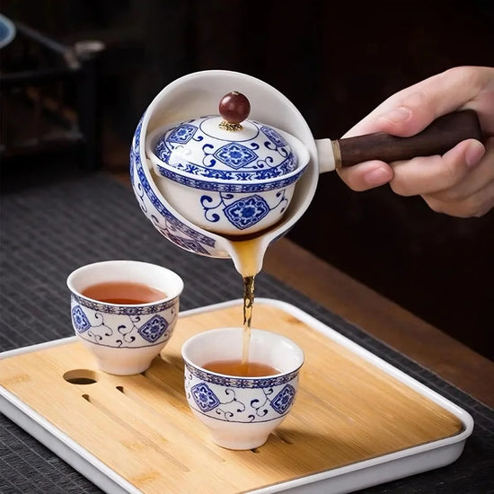 Blue and white porcelain teapot pouring tea into matching ceramic cups on a wooden tray