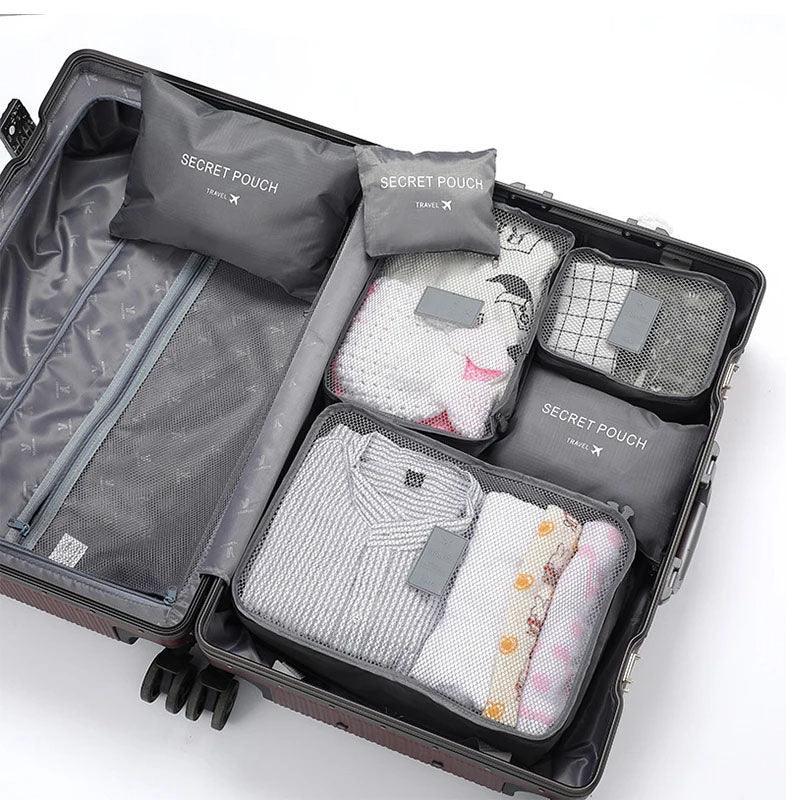 Open suitcase with neatly packed gray mesh travel pouches, folded clothes in light colors.