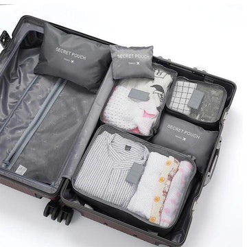 Open suitcase with neatly packed gray mesh travel pouches, folded clothes in light colors.