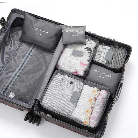 Open suitcase with neatly packed gray mesh travel pouches, folded clothes in light colors.